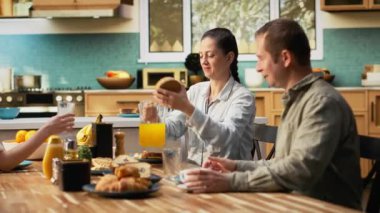 Aile zengin bir kahvaltı için mutfak masasının etrafında toplandı, hamur işi ve taze portakal suyunun tadını çıkardılar. Ebeveynler ve kızları arasındaki yemek sırasında neşeli sabah röfleleri. Kamera B.
