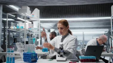Laboratuvar geliştirme uzmanı test tüpüne mavi sıvıyı koyup analiz ediyor. Moleküler biyolog, spektroskopik analize hazırlanmak için kimyasal örnek transfer ediyor. Kamera A.