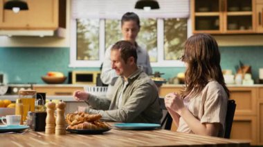 Gülümseyen ebeveynler ve iki çocuk kahvaltı masasında waffle ve taze yemekle bir araya geldiler. Mutfak sahnesi sabah bağlantısını, aile bağlarını ev yemeğini paylaşmak için gösteriyor. Kamera B.
