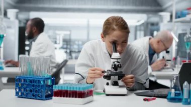 Tıbbi laboratuvardaki moleküler biyolog hücresel analiz için bilimsel mikroskop kullanıyor. Laboratuvarda optik cihaz teçhizatı ve kamera B ile örnek inceleme yapan kadın araştırmacı.