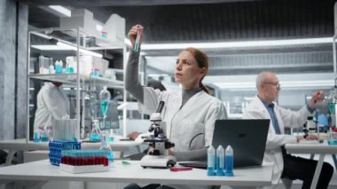 Tıbbi laboratuvar teknisyeni test tüpündeki mavi sıvı kimyasal özellikleri inceliyor. Araştırma tesisi çalışanı yeni bileşik içeren şişeyi tutuyor. Tıbbi araştırma ve araştırma yapıyor. Kamera A.