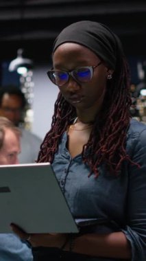 Laptop kullanan dikey video kadın teknisyeni yapay zeka sistemindeki hataları düzeltmeye çalışıyor. Teknoloji ajansının işyerindeki kadın sinir ağı hatalarını not defteriyle gideriyor