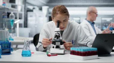 Patolojiyi inceleyen tarih teknisyeni mikroskop altında slayt inceliyor, çalışma masasındaki kötü duruşu düzeltiyor. Tıbbi yenilikleri hücresel analiz yoluyla yürüten araştırmacı sırt ağrısı çekiyor, kamera B