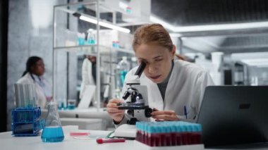 Patolojiyi inceleyen tarih teknisyeni mikroskop altında slayt inceliyor, çalışma masasındaki kötü duruşu düzeltiyor. Hücresel analiz yoluyla tıbbi yenilikleri yürüten araştırmacı sırt ağrısı çekiyor, kamera A