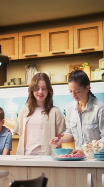 Dikey Video Neşeli Aile Bağlanması ve mutfakta birlikte ev yapımı pizza pişirmek, malzemelerden önce hamur üzerine sos eklemek. Aileler ve çocuklar hafta sonları kahkahalarla eğleniyorlar. Kamera A