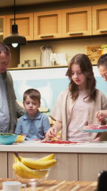 Pizza günü ebeveynler ve çocuklarla mutfakta dikey video aile zamanı mozzarella ve pepperoni gibi malzemeler ekleniyor. Eğlenceli ve lezzetli ev yemekleri, kahkahalarla çevrili. Kamera A.