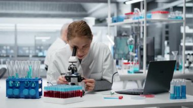 Patoloji slaytlarını inceleyen gülümseyen bilim adamının portresi araştırma merkezinde mikroskop altında. Mutlu kadın kendini adamış hücresel analiz çalışmaları ve kamera B ile tıbbi yenilikler yapıyor.