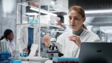 Klinik teknisyeni hasta biyopsi slaytını inceleyerek anormal hücresel büyümeyi tespit ediyor. Teşhis doğrulaması için hastane laboratuvarında yüksek teknolojili mikroskop kullanan kadın, kamera B