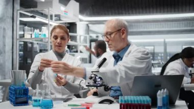 Laboratuar şefi stajyere test tüpünde sıvı polimer özelliklerini analiz etmeyi öğretiyor. Kıdemli bilim adamı, laboratuarda yeni sentetik materyal viskozitesini test etmek için stajyere danışmanlık yapıyor. Kamera A.