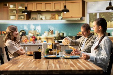 Annem ve babam waffle ve taze ev yemeği yemek için kızımla kahvaltı masasında toplandılar. Mutfak sahnesi sabah bağlantısını gösteriyor, aile bağlarını ev yemeğini paylaşmak için..