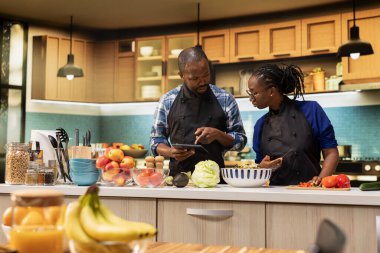 Siyahi sevgili, internette yemek tarifi içeren bir yemek hazırlıyor, malzemeleri kesiyor ve mutfakta vejetaryen salatası yapıyor, sağlıklı bir yaşam tarzı ve aşçılık yapıyor..