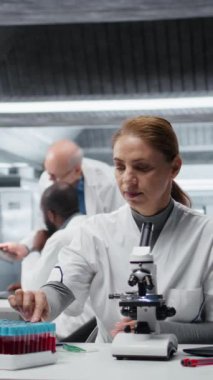 Dikey video hematoloji uzmanı. Laboratuvarda kan örneği üzerinde araştırma yapıyor, not alıyor. Laboratuvarda epidemiyoloji uzmanı şişedeki sanguin sıvısı örneğini analiz ediyor, bulguları yazıyor, kamera A