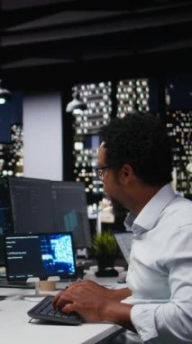 Dikey video teknisyeni gece vardiyası sırasında yüksek katlı ofiste yapay zeka algoritmaları geliştiriyor. Afrika kökenli Amerikalı adam sinirsel ağ beyin modellerini ekranlarda, kamera A 'da hata ayıklıyor.