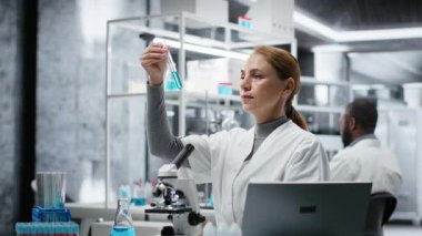 Laboratuvardaki bilim adamları analiz etmek için mavi sıvıyı test tüpüne koyuyorlar. Laboratuvar çalışanı spektroskopik analize hazırlanmak için kimyasal örnek aktarıyor. Kamera B.