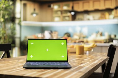 Mutfaktaki laptopta yeşil ekran ve kırsal sayaç ve zarif ışıklandırma. Mutfak eşyaları ve çatal bıçakları modern iç tasarım ile konforlu ve davetkar bir ev yemeği alanı yaratıyor..