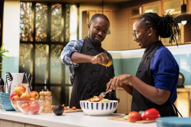 Sebzelerin üzerine limon suyu sıkan genç siyahi bir adam ve kadın malzemeleri bir kasede karıştırıyor, insanlar mutfakta salatayı birlikte hazırlıyorlar. Romantik sağlıklı yaşam tarzı.