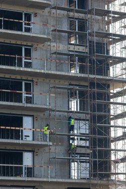 Facade installers attach thermal insulation panels to exterior concrete wall of multi story complex. Construction team of cladders on scaffolding platform working to improve apartments