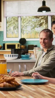 Dikey Video Ailesi kahvaltıda omlet ve hamur işi paylaşıyor, ebeveynler küçük oğlan ve küçük kızla omlet ve tost servisi yapıyor. Sıcaklık, rahatlama ve neşe dolu birliktelik. Kamera.