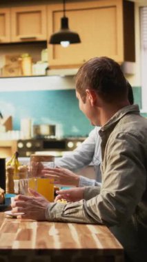 Dikey Videocu Kadın, genç kız ve kocası için bardağa portakal suyu dolduruyor, ev yemeği hazırlıyor ve taze hamur işlerinin tadını çıkarıyor. Aile birlikte sabahları eğleniyor, sevgi gösteriyorlar. Kamera A.