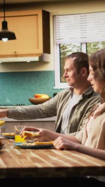 Dikey Video Ailesi mutfakta kahvaltı servisi yapıyor ve portakal suyu dolduruyor. Yumurta ve pastanın tadını birlikte çıkarıyorlar. Sabah rutini, hafta sonu yemekte paylaşılan neşe ve sevgiyle dolu. Kamera A.