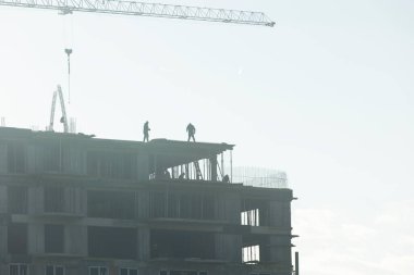 İnşaat alanındaki müteahhitler, güneşli bir günde yeni binalar inşa etmek için ağır makineler kullanıyorlar. Crane operatörü tamamlanmamış uzun apartman kompleksi, dikey şehirleşme kavramı üzerinde çalışıyor.