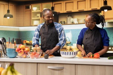 Gülümseyen kadın ve erkek sebze kesiyor ve kesme tahtasındaki malzemeleri düzenliyor, birlikte yemek pişiriyorlar. Salata kasesi için organik sebze doğrayan çiftler, gevşetilmiş eğlence enerjisi..