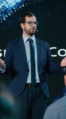 Dikey video modern konuşmacı sahnede iş konferansı sırasında motivasyon konuşması yapıyor. Çeşitli profesyoneller ve beyaz yakalı işçiler konferans salonundaki uluslararası etkinliğe katıldılar