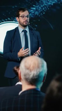 Sahnedeki Dikey Video İşadamı, iş konferansında seyircilere hitap ediyor, ilham verici bir konuşma yapıyor. Profesyonel seyirciler şirket zirvesine liderlik odaklı olarak katıldılar