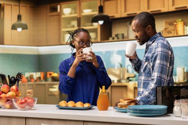 Siyah erkek arkadaş ve kız arkadaş mutfakta taze kahve içip sohbet ediyorlar, kruvasan ve tost hazırlıyorlar. Mutlu hafta sonu sabahı aşk ve sağlıklı ev yapımı kahvaltı ve yaşam tarzıyla dolu.