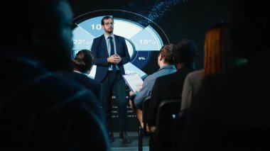 İş adamı sahnede, iş konferansında seyircilere hitap ediyor, ilham verici bir konuşma yapıyor. Profesyonel seyirciler yönetim odaklı şirket zirvesine katıldılar. Kamera A.