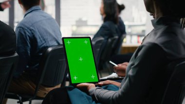 Dik yeşil ekran tableti kurumsal iş forumunda, sahnede konuşma yapan kişi tarafından tutuldu. Beyaz yakalı işçilerden oluşan çeşitli seyirciler panel etkinliği sırasında dinliyorlar.