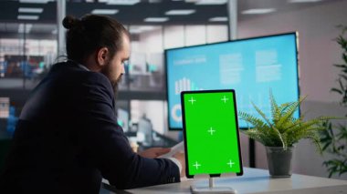 İş adamı KPI 'lerin analiz edildiği tablet üzerinde dikey krom anahtar, veri yönetimi için günlük görevler ve raporlar değerlendirmesi. Kârlılık ve yönetimle ilgili belgeler.