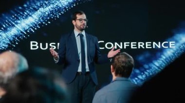 Erkek modern konuşmacı iş konferansı zirvesinde motivasyon konuşması yapıyor. Çeşitli profesyoneller ve beyaz yakalı işçiler konferans salonundaki uluslararası etkinliklere katıldılar. Kamera B.