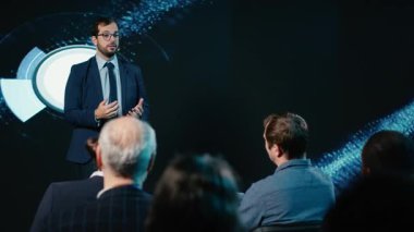 İş adamı sahnede, iş konferansında seyircilere hitap ediyor, ilham verici bir konuşma yapıyor. Profesyonel seyirciler yönetim odaklı şirket zirvesine katıldılar. Kamera B.