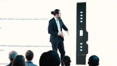 Erkek CEO, modern akıllı telefon arayüzünün prömiyeri ile sahnede yeni cep telefonu ürünü tanıtımını sunuyor. Girişimci ürün piyasaya sürerek yenilik ve geliştirme sunar. Kamera B.