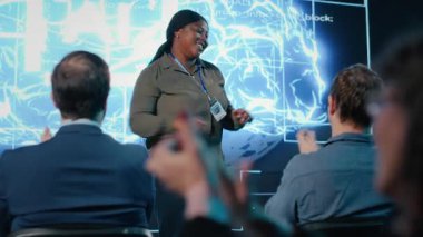 Siyahi kadın, yapay zeka özellikleri ve yapay zeka çözümleri sergileyen teknoloji forumuna ev sahipliği yapıyor. Uzman konuşmacı katılımcılar ve çeşitli izleyicilerle iş tartışmasına öncülük ediyor. Kamera B.