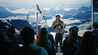 Siyah kadın konuşmacı rüzgar enerjisi sunumunu rüzgar türbini makinesi ve rotasyonuyla iş konferansında yapıyor. Halka hitaben yaptığı konuşmada dinleyicilere alternatif enerji üzerine konuşma yapmak. Kamera A.