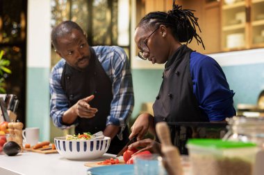 Siyahi genç aşıklar sebze doğruyor ve kesme tahtasındaki malzemeleri hazırlıyor, birlikte yemek pişiriyorlar. Salata kasesi için organik sebze kesen çift, evde gevşemiş eğlence enerjisi..