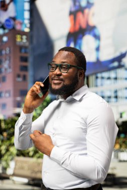 Kalabalık şehir caddesinde telefonla konuşan siyahi bir insan modern mimari ile günlük yaşam tarzını ve sokak tarzını sergiliyor. Çevresindeki şehir hayatının dinamik ritmi.