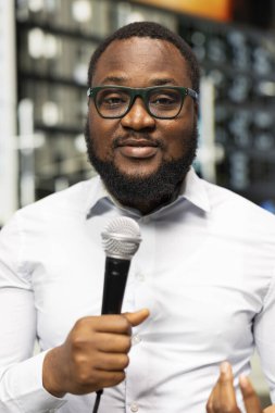 Erkek muhabirin mikrofonla canlı yayında konuşmasını, saha çalışması yapmasını ve son dakika haberini iletmesini kapatın. Açık şehir ortamında rapor verirken net bir yorum sunuluyor.