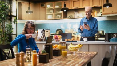 Yetişkinlerin akıllı telefonlarıyla internete bakması, mutfakta gülümsemesi, kahveyle rahatlaması ve huzurlu emeklilik hayatının tadını çıkarması. Emeklilik, pozitif yaşam tarzı ve rutin. Kamera A.