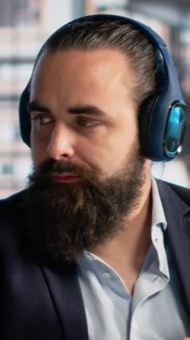 Dikey Video İşadamı, yönetici ofisinde müzik dinleyerek ve dans ederek iyi ruh hali ve stres atışıyla birden fazla iş yaparak eğleniyor. Profesyonel kulaklıklı, neşeli ve kaygısız.