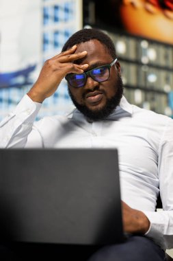 Siyah yetişkin insan parktaki bankta çalışırken yorgun ve hayal kırıklığına uğramış, kötü haberlerden rahatsız olmuş ve sıkılmış. Şehir merkezindeki kalabalık gökdelenlerle çevrili.