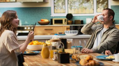 Tablette gülümseyen baba küçük kızıyla sohbet ediyor, ailesiyle kahvaltı yapıyor ve mutfakta güzel ev yemekleri yiyor. Beraberlik ve neşe.