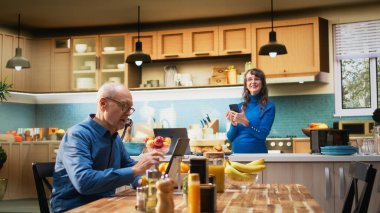 Yaşlı ev hanımı mutfaktaki tezgahın yanındaki cep telefonuyla evde sakin bir anın tadını çıkarıyor. Huzurlu bir yaşam tarzı, sağlıklı bir yaşam ve emekli olmanın keyifli rahatlığını yansıtıyor. Kamera A.
