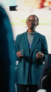 Dikey Video Siyah Kadın, kurumsal etkinlik sırasında dinamik sosyal medya sunumunu yönetiyor ve iş adamlarına sesleniyor. Kadın sunucu markalaşma ve dijital iletişim hakkında görüşlerini paylaşıyor