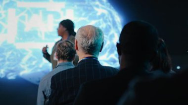 Yaşlı işadamı konferans salonundaki yapay zeka sunumuna katılarak seyircilerden siyahi kadın sunucuyu dinliyor. Otomasyon yazılımı ve yeni teknoloji. Kamera B.