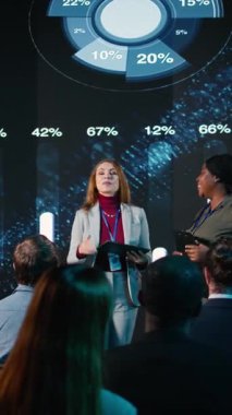 Dikey Video Çoklu Etnik Kadın Yetişkinler, dijital ekranda pazar payı eğilimleriyle bir panel tartışmasına ev sahipliği yaparken, sunucular ekonomi iş sektörü için sermaye numaralarını gösteriyor. Şamdanlar çizelgeleri