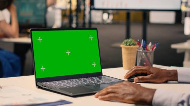 İş yerinin masasında oturan siyah bir adamın yeşil ekran modeli günlük işlerin kurumsal yaşam tarzı görüntüsü. Raporlar ve analitik gösterge paneli stratejik planlama ve hedefleri destekliyor.