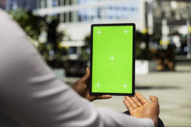 Tabletteki dikey maket ekranda parktaki bankta oturan siyah bir adam gökdelenlere ve metropoliten alan titreşimlerine hayran. Kendine güvenen duruş ve kaldırım manzarası için modern sokak tarzı.